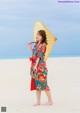 A woman in a colorful kimono holding an umbrella on the beach.