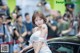 A woman sitting on top of a car in front of a crowd.
