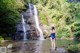 A woman in a blue bathing suit standing in front of a waterfall.