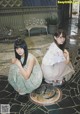 Two young women sitting on the ground in front of a building.