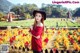 A woman in a red sweater and black hat standing in a field of flowers.